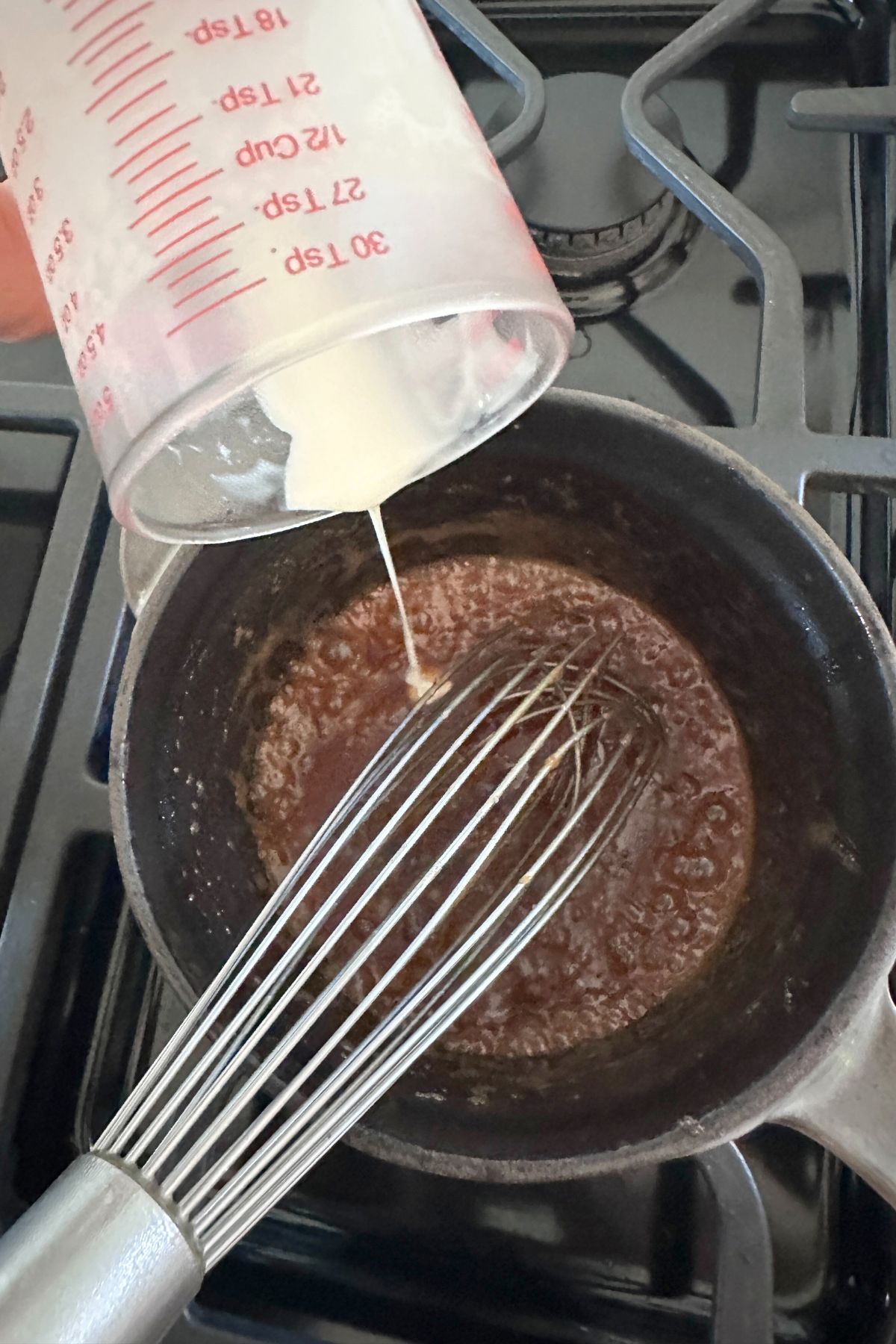 Melted butter and brown sugar in a medium saucepan as cream is poured in, ready to be whisked together.