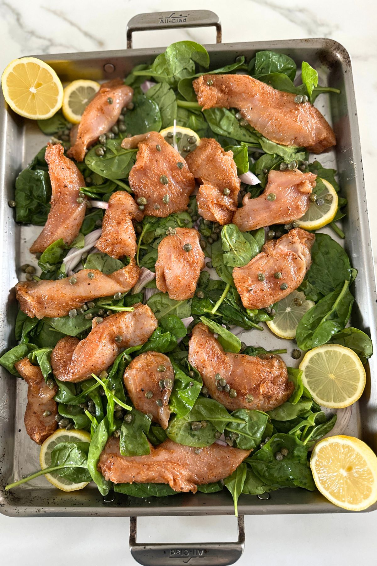 Seasoned chicken added to the sheet pan with capers, wine, and chicken stock.
