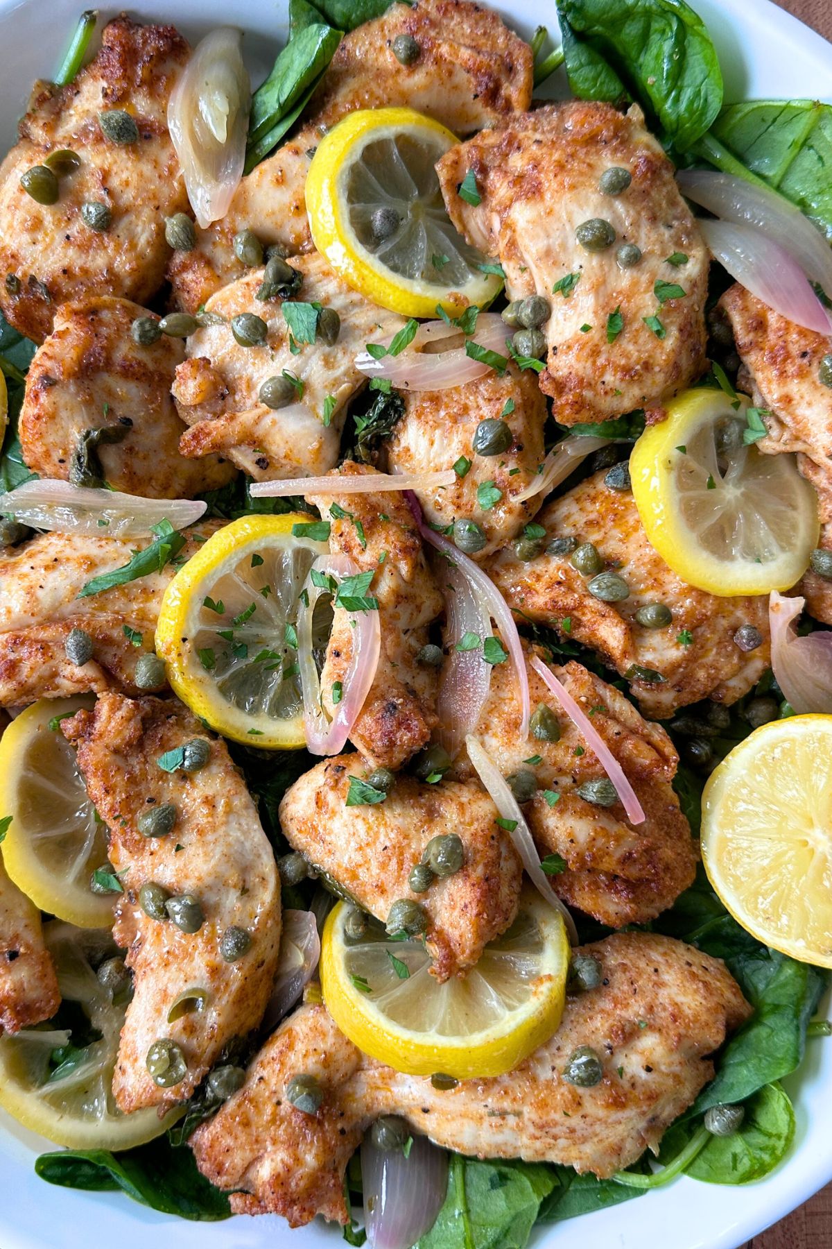 Close-up of sheet pan chicken piccata topped with capers and fresh lemon slices.