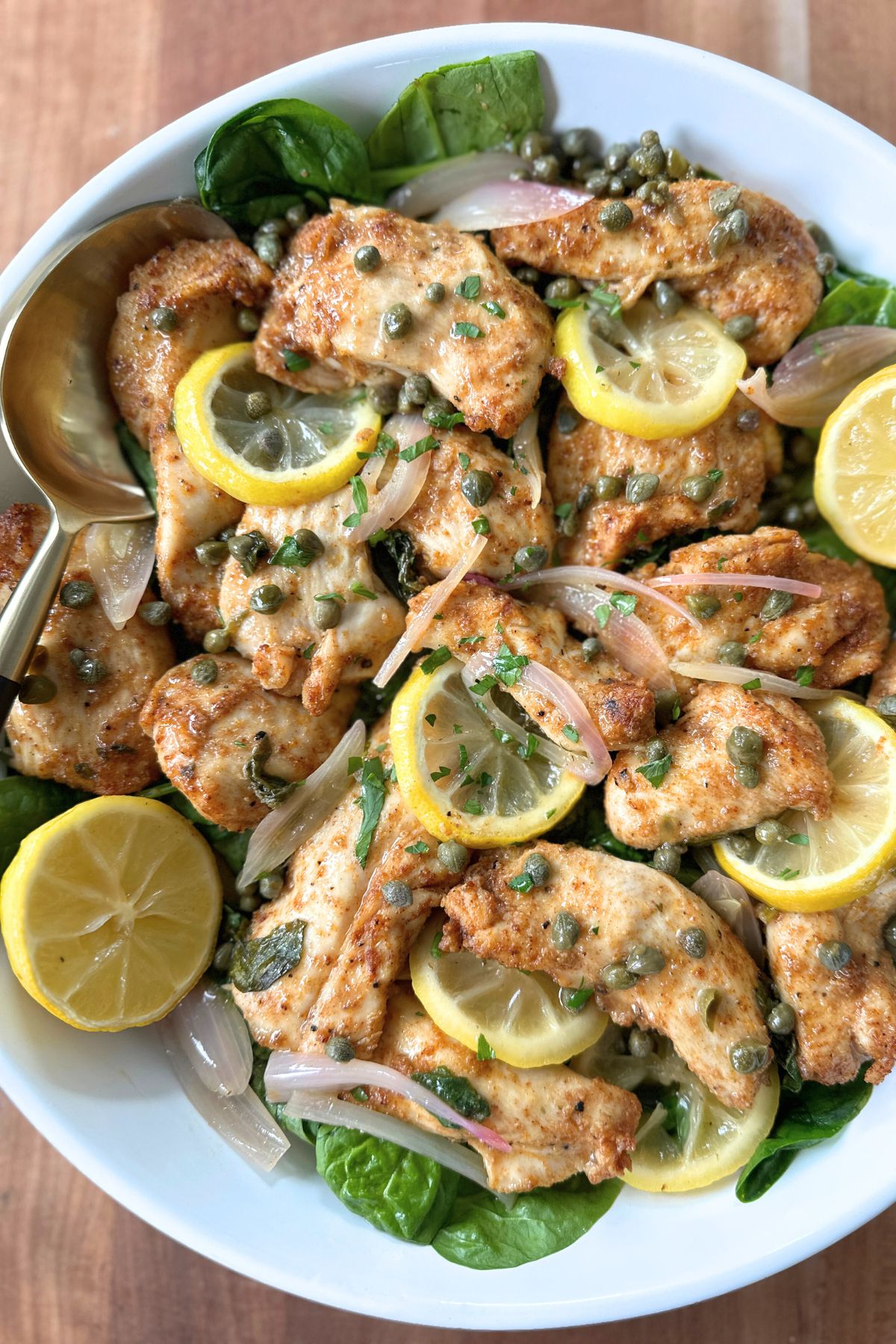 Sheet pan chicken piccata with lemons, capers, spinach, and shallots on a white plate, ready to eat.