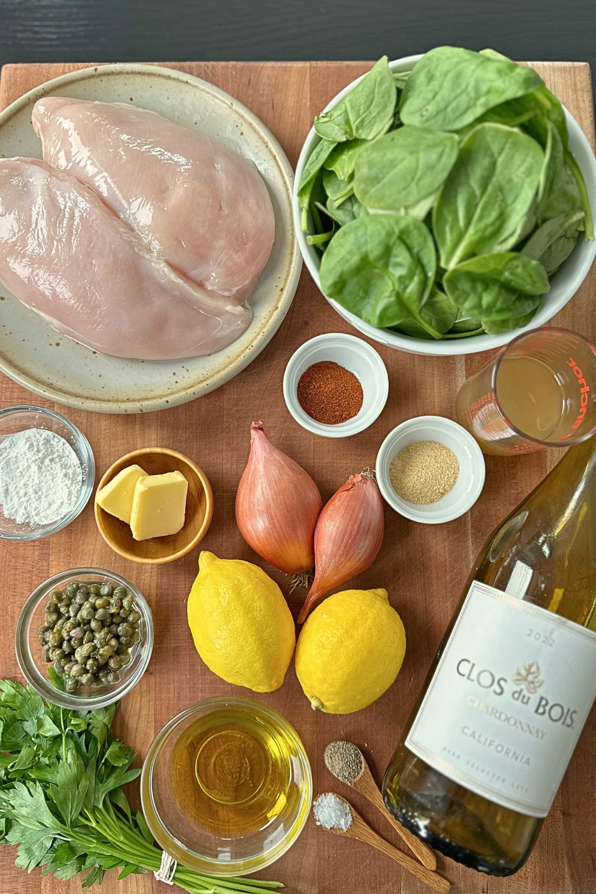 Measured ingredients for sheet pan chicken piccata arranged on a wooden cutting board.