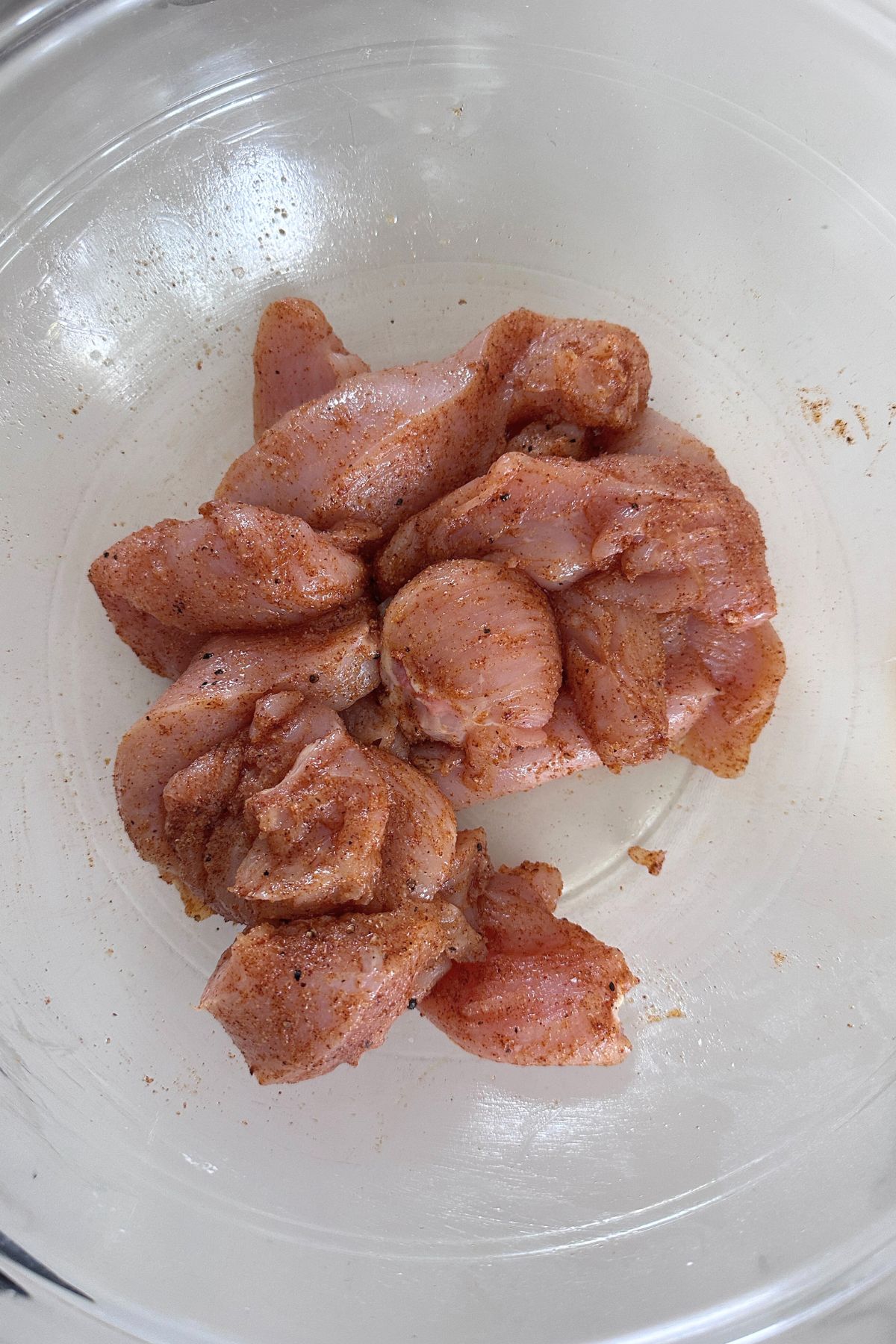 Raw chicken tossed with spices and arrowroot in a glass bowl.