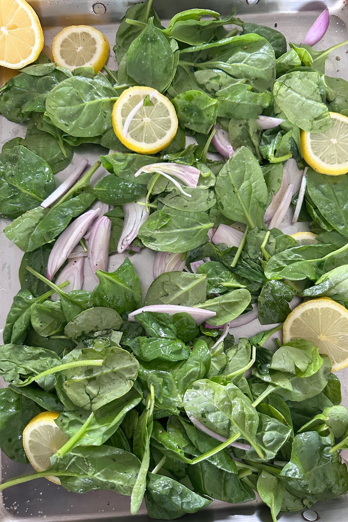 Shallots, spinach, and lemon slices arranged on a greased sheet pan.