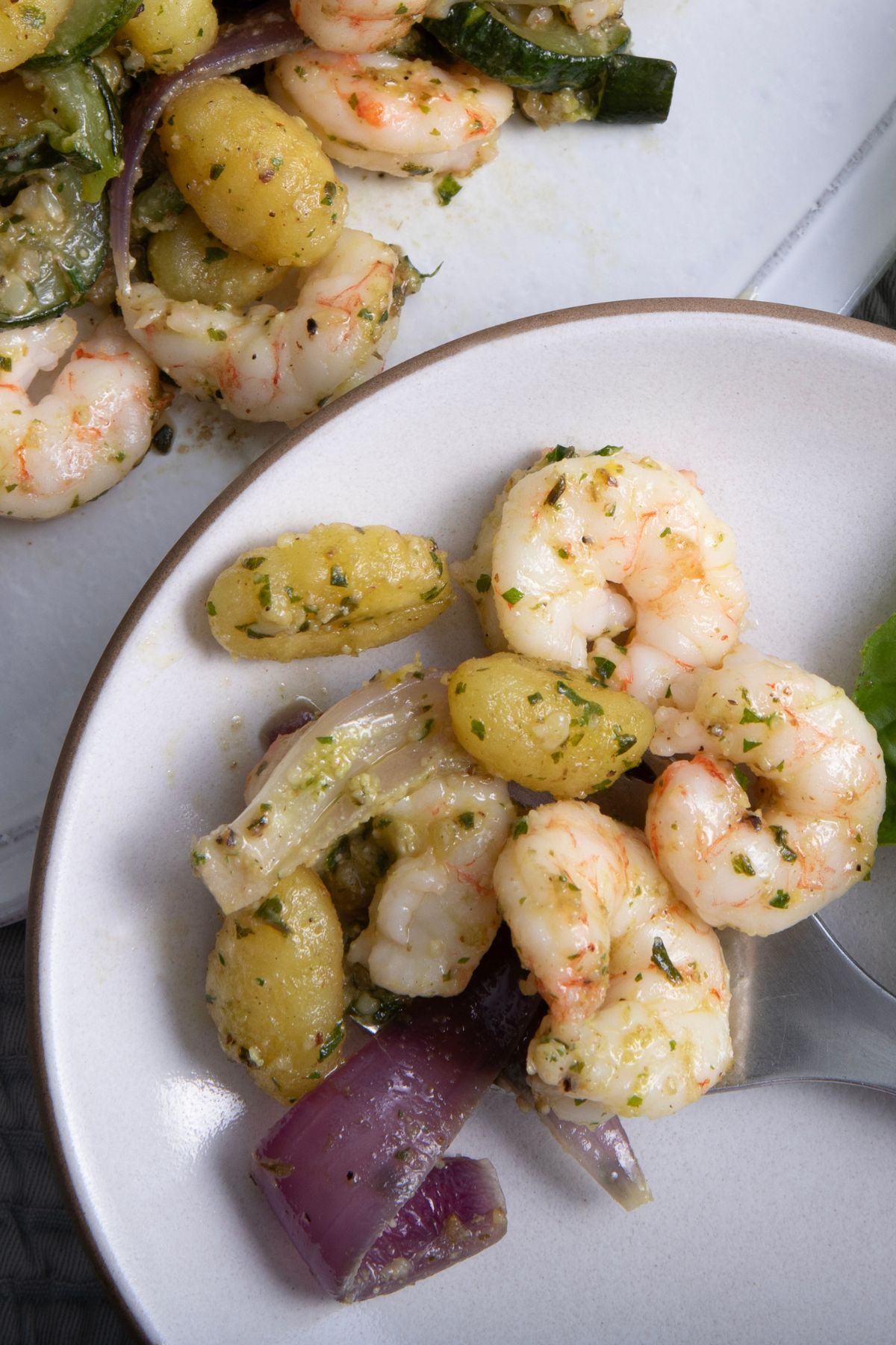 Finished sheet pan gnocchi with shrimp, vegetables, and pesto served in a large white bowl.