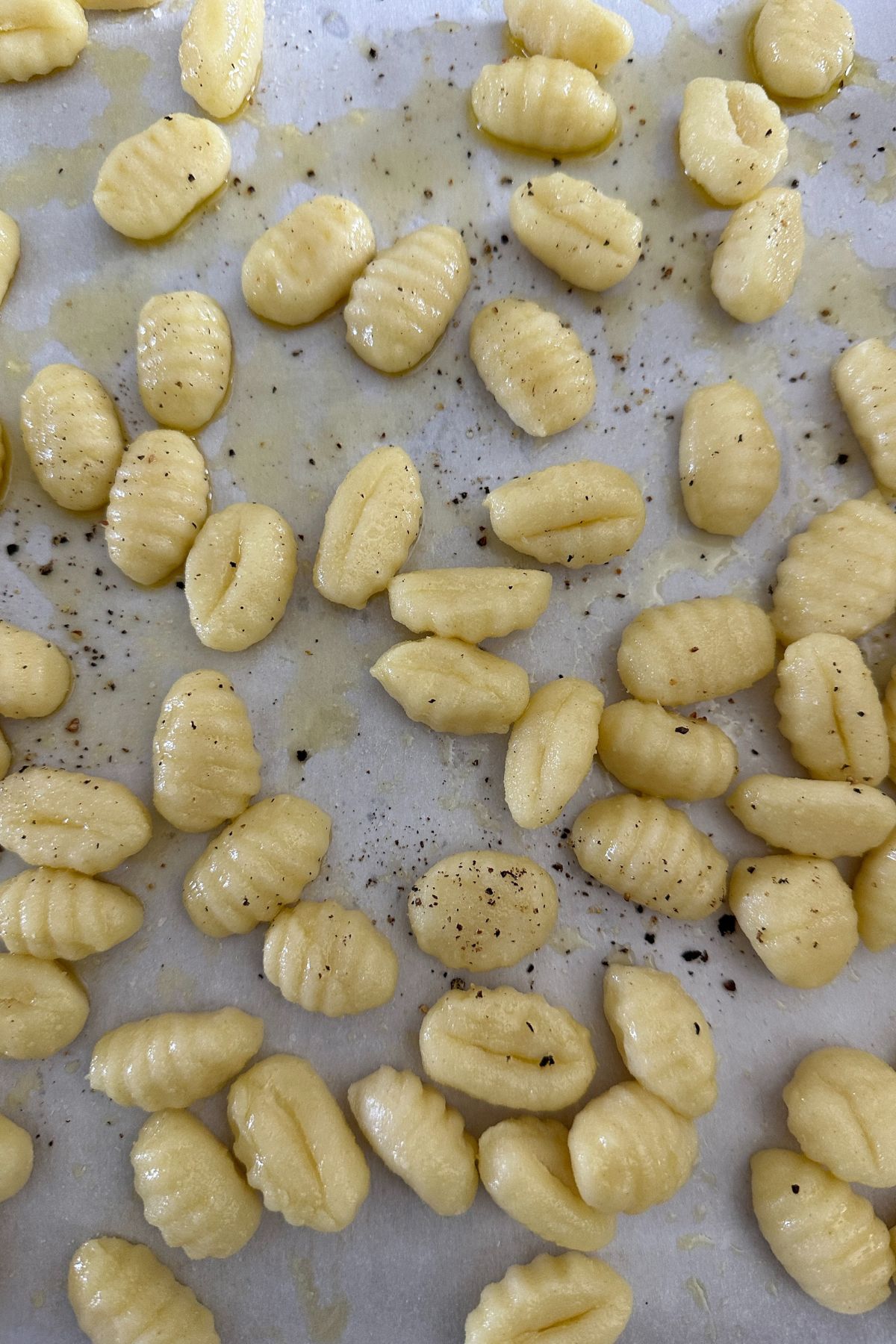 Uncooked potato gnocchi spread on a parchment-lined sheet pan, drizzled with olive oil, and ready for roasting.