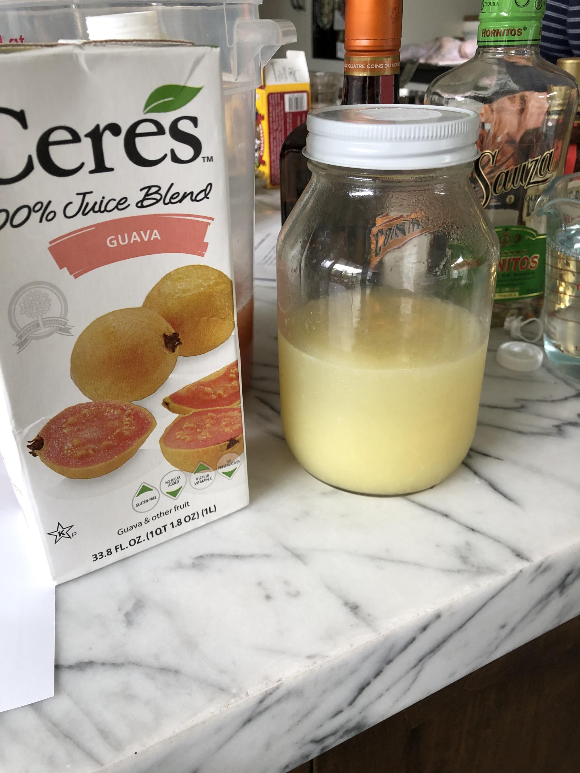 Spicy margarita ingredients including tequila, orange liqueur, lime juice, guava nectar, and fresh jalapeños on a table.