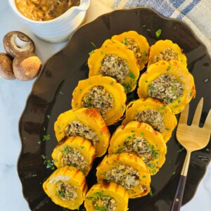 Stuffed delicata squash arranged on a black serving platter with a large fork lying next to them.