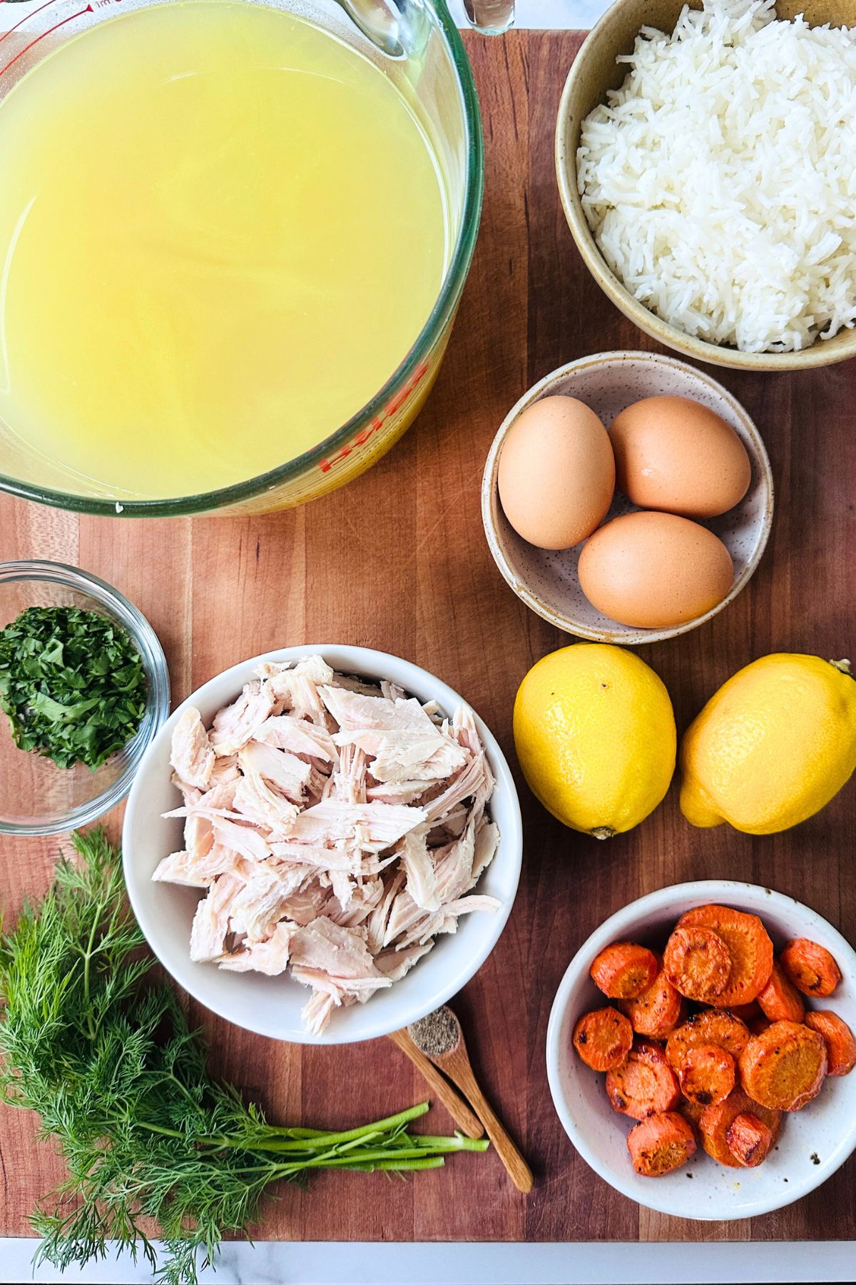 Avgolemono soup recipe ingredients laid out on a wooden cutting board.