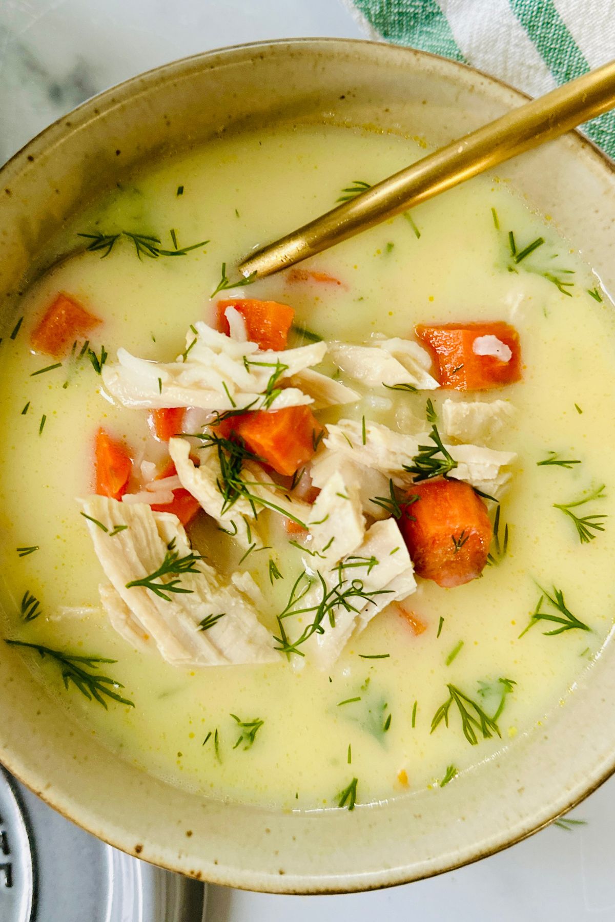 Close-up of a small bowl of avgolemono soup with a spoon resting inside, showing the leftover turkey and carrots.