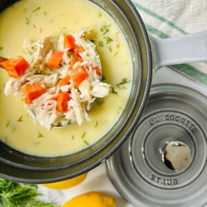 A large gray Dutch oven filled with avgolemono soup, with a ladle lifting a scoop that shows the leftover turkey, carrots, and cooked rice.