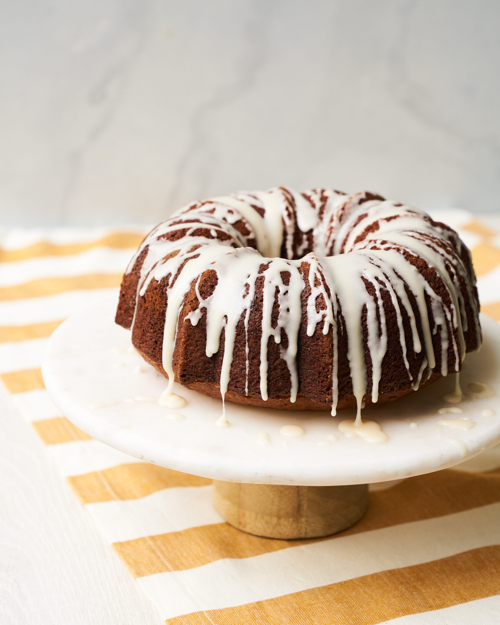 Apple bundt cake displayed on a cake stand atop a yellow and white striped tablecloth.